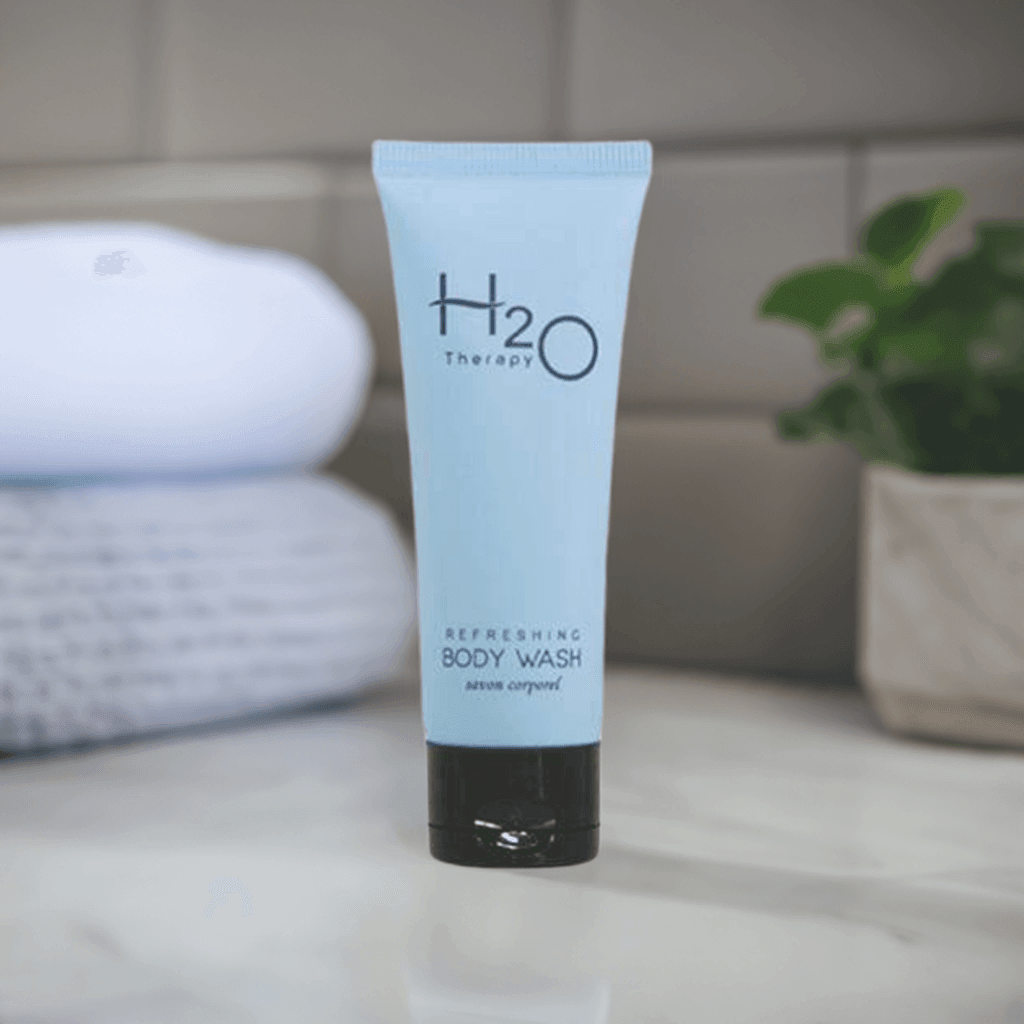 H2O Therapy Refreshing Body Wash tube on marble countertop with towels and plant background