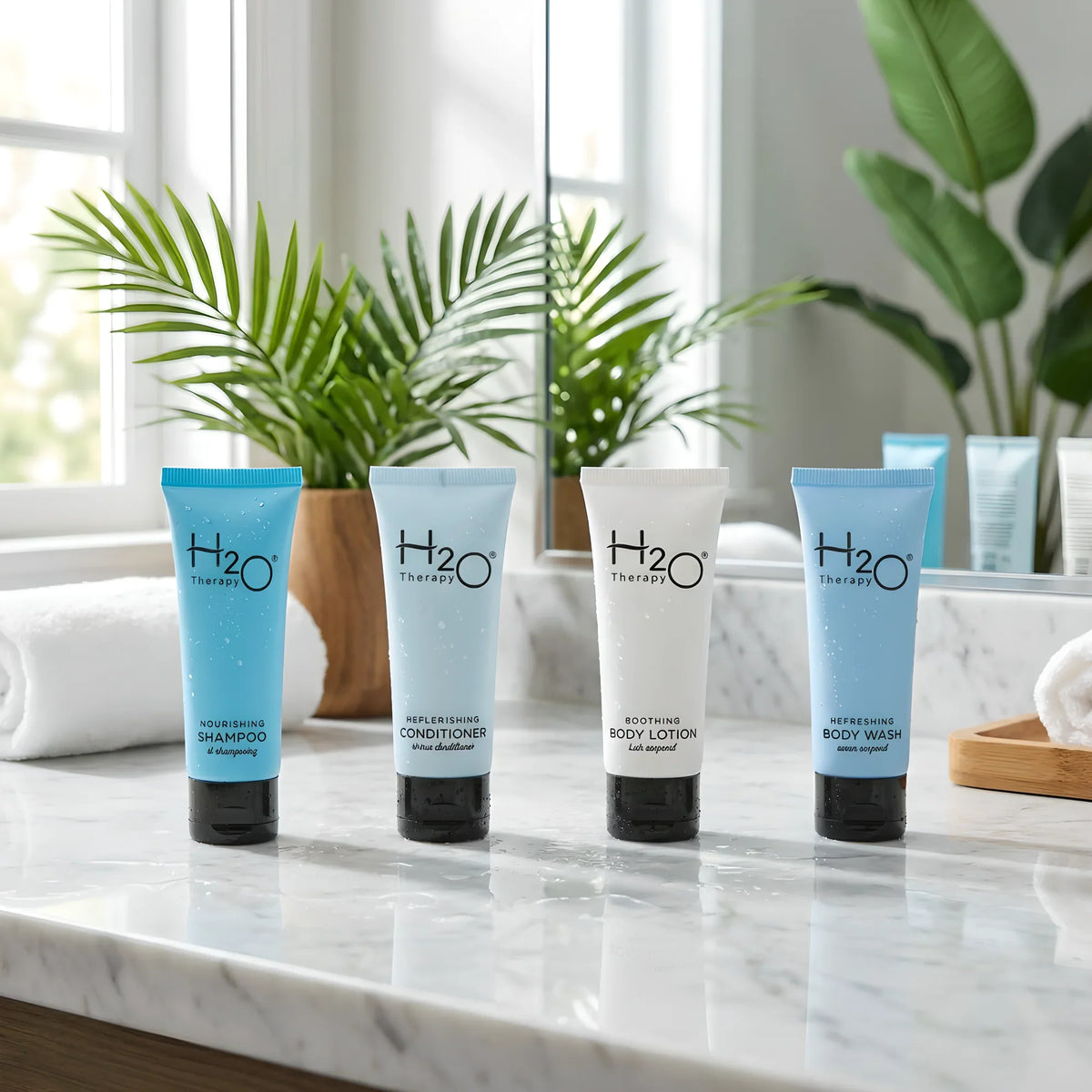 H2O Therapy hotel amenities: shampoo, conditioner, body lotion, body wash on marble counter with plants